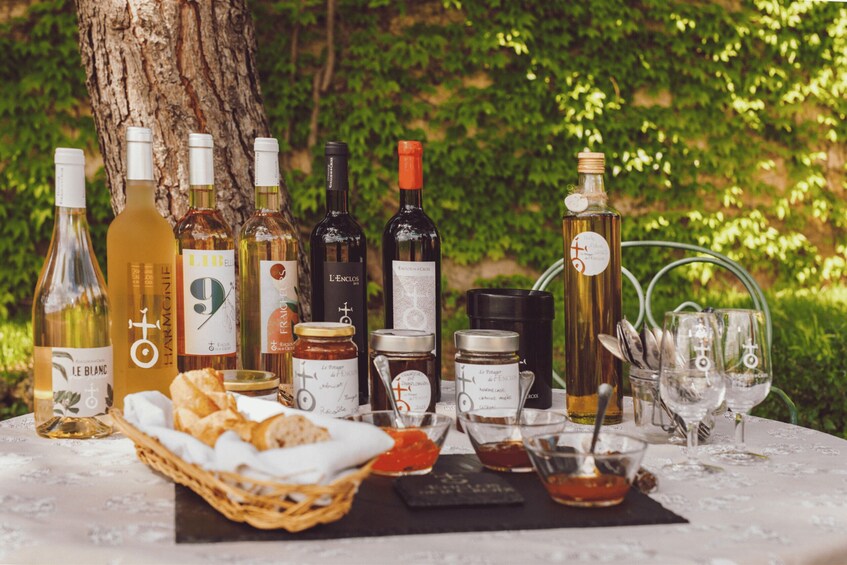 A table with various bottles of wine and glasses, set outdoors with a tree and greenery in the background. 3
