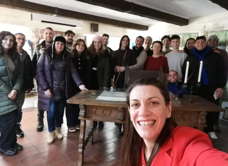 Un groupe de personnes se tient autour d’une table éclairée par des bougies, dans une pièce dont le sol est recouvert de carreaux et dont le plafond est orné de poutres en bois. 3