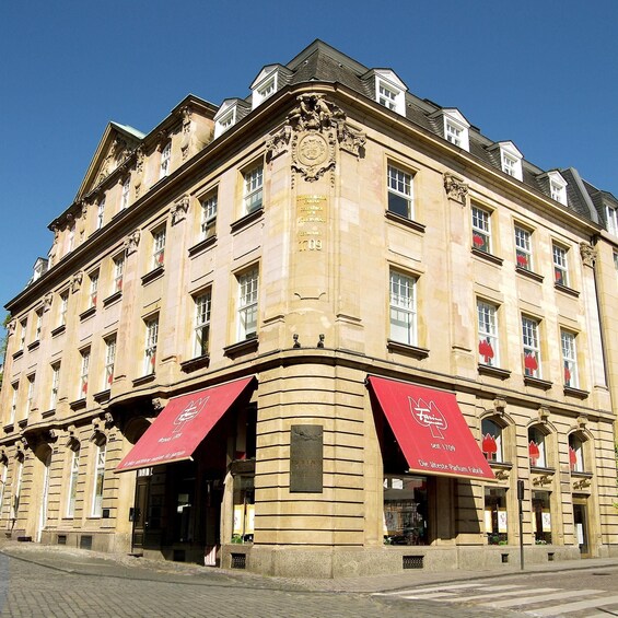 Un bâtiment historique à l’architecture riche et travaillée, doté de grandes fenêtres et de marquises rouges. 1