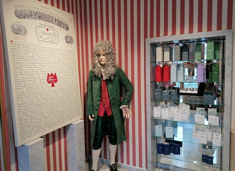 Un mannequin vêtu d’un costume d’époque, placé à côté d’une collection de flacons de parfum et d’un document historique. 4