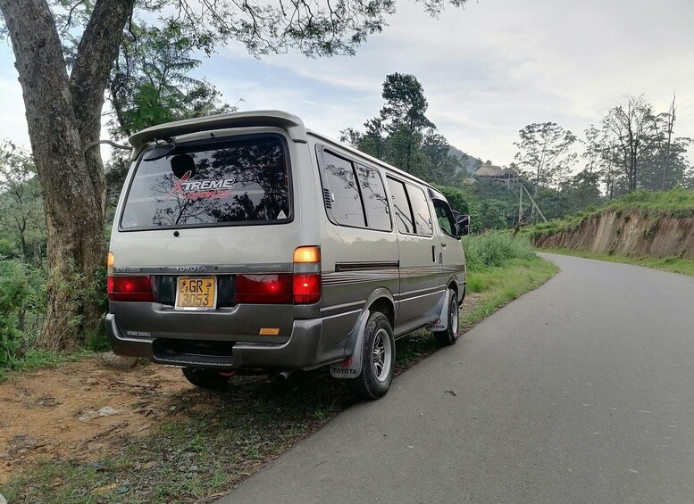 A Toyota van parked on a rural road with trees and a hill in the background. 2