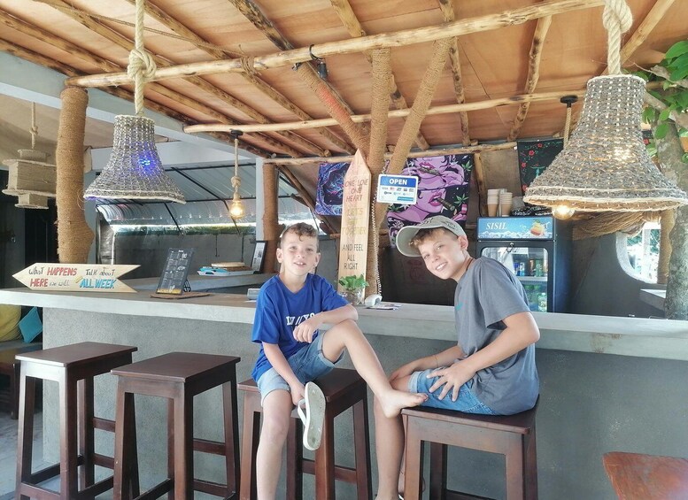 Two people sitting at a wooden bar with a rustic ceiling, a sign that says 'What Happens Here,' and a SisiL beverage machine. 1