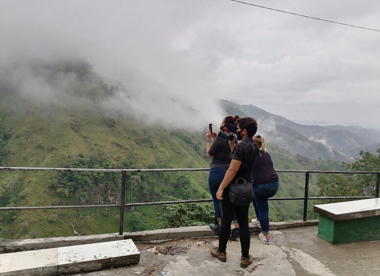 A group of people taking a photo of a mountainous landscape with a railing in the foreground. 5