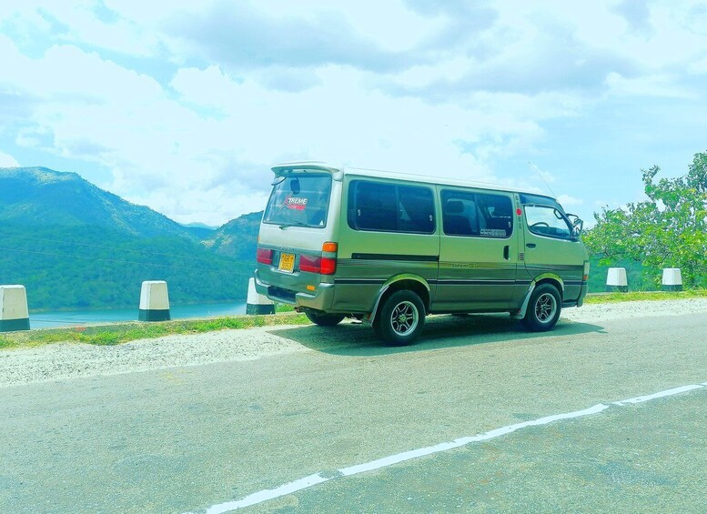 A green van parked on a road with a lake and mountains in the background. 4