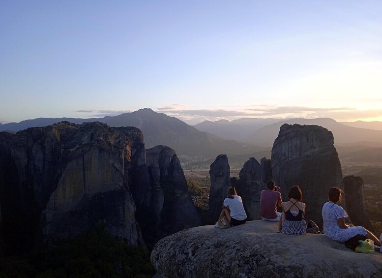A group of people sitting on a rock overlooking a mountainous landscape. 4