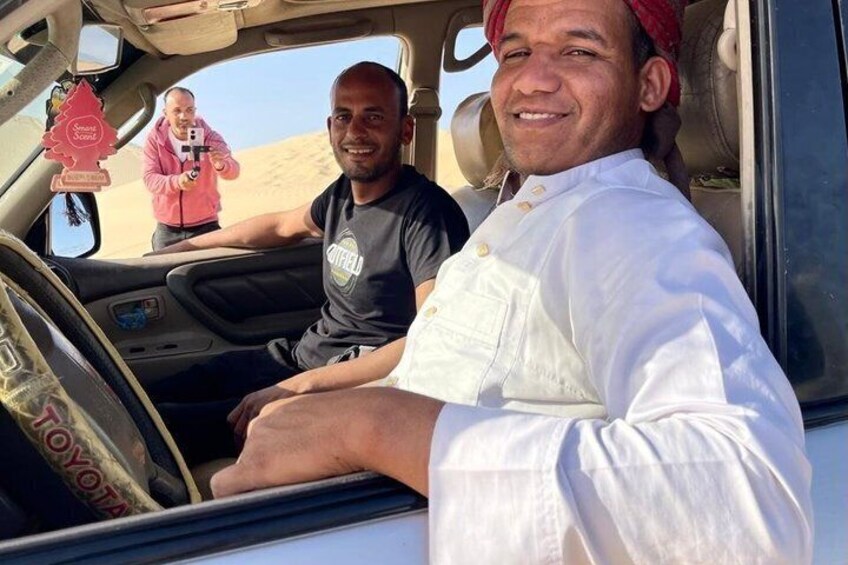 A person in a white shirt sitting in a vehicle with a desert landscape in the background. 3