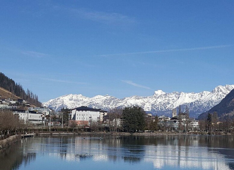 A calm lake with reflections, snow-capped mountains in the background, and buildings along the shore. 4