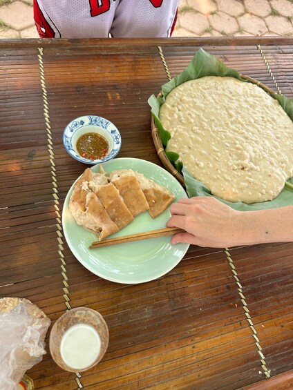 A meal with a large pancake, a plate of sliced meat, a bowl of sauce, and a small cup of milk on a wooden table. 2