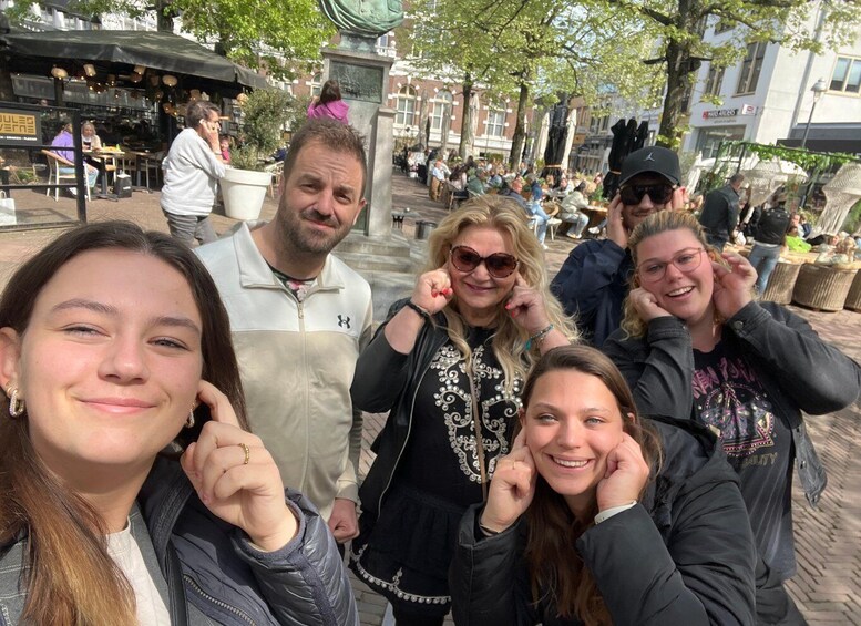 A group of people posing for a photo in a public square with outdoor seating and trees. 1