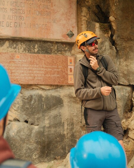 A person in a helmet and jacket standing next to a stone wall with inscriptions. 2