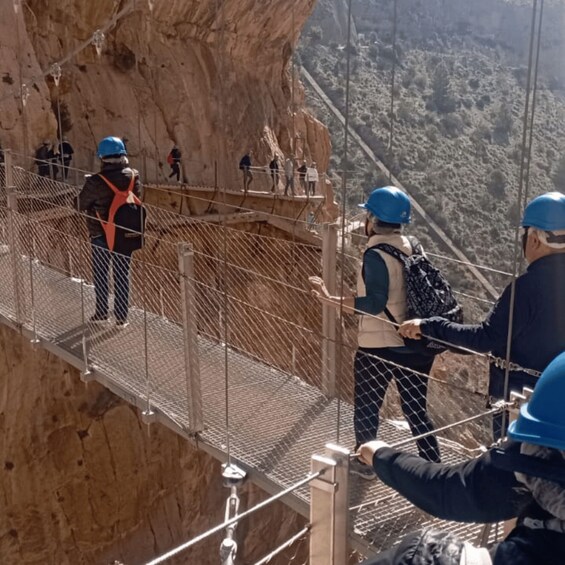 A group of people on a suspended bridge with safety railings, overlooking a mountainous landscape. 3