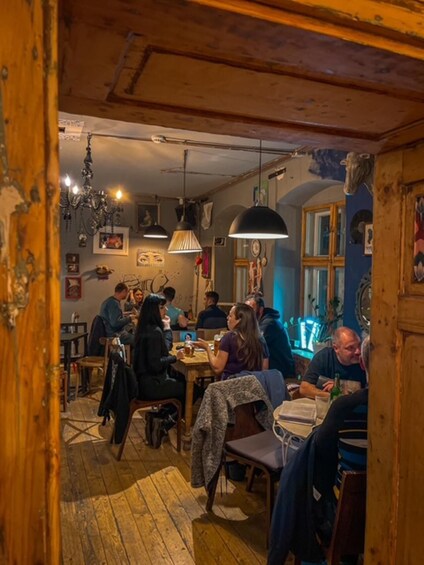 A rustic interior with wooden beams, a chandelier, and patrons dining at tables. 3
