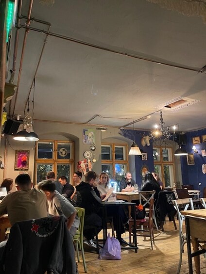 A restaurant interior with patrons seated at tables, wooden floors, and hanging lights. 2