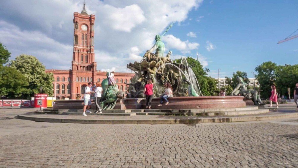 A historic tower, a large fountain sculpture, and cobblestone pavement. 3
