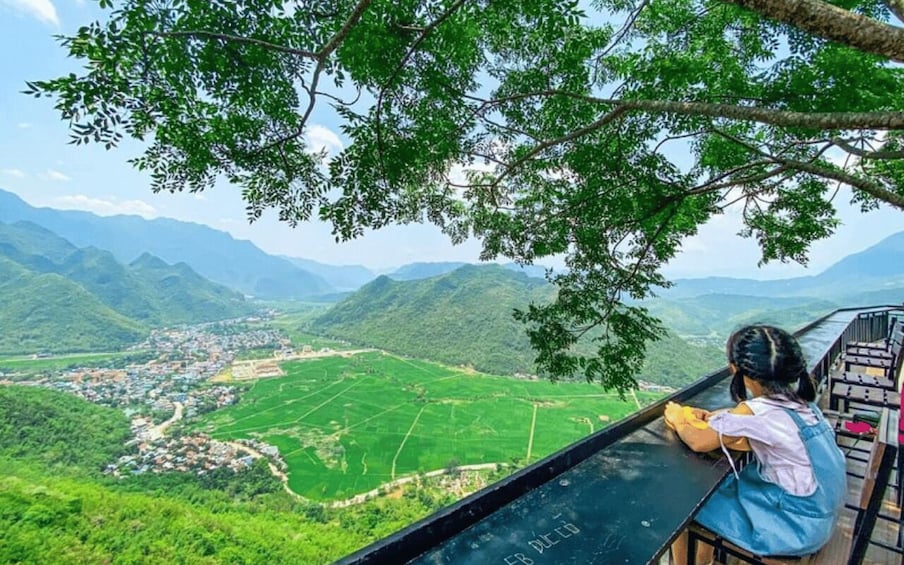 A person overlooking a valley with green fields and mountains in the distance. 1