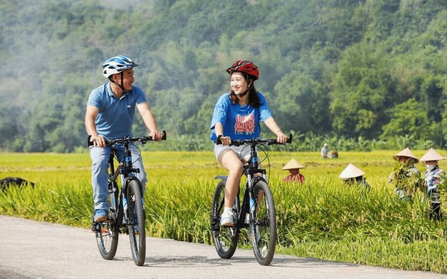 Two people riding bicycles on a path with a rural landscape in the background. 3