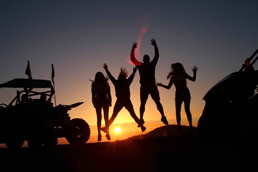 Silhouettes of people jumping against a sunset with ATVs in the foreground. 4