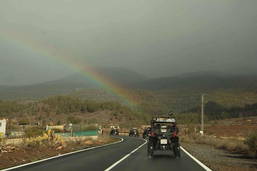 A road with vehicles, a rainbow, and a mountainous landscape. 5