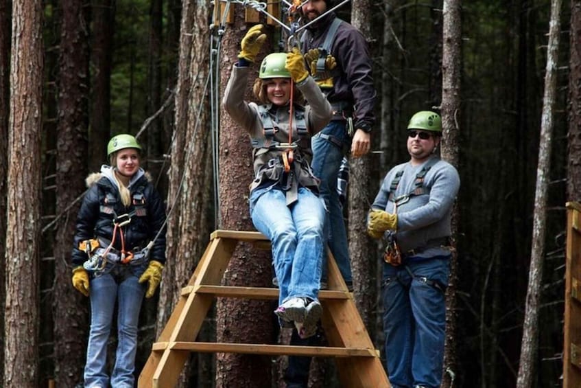 A person on a zip line in a forest, with others assisting. 5