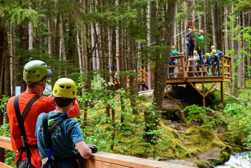 A group of people on a wooden platform in a forested area with a river below. 2