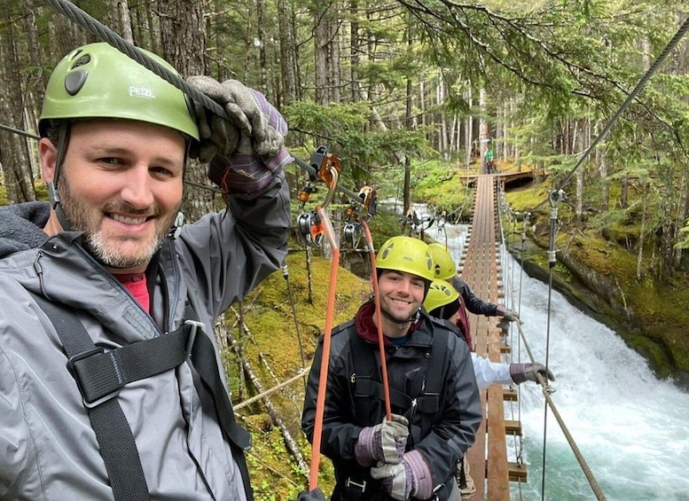 A person wearing a helmet and harness on a suspension bridge over a river in a forest. 4
