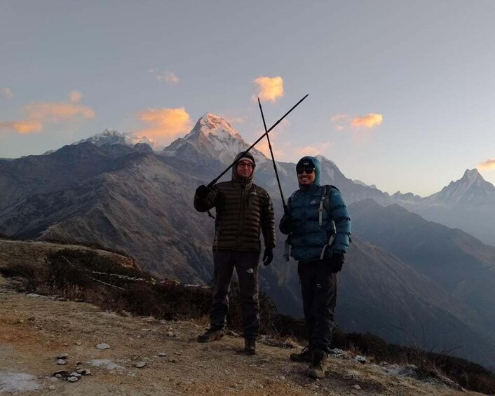 Two people standing on a mountain ridge with a view of snow-capped peaks in the background. 4