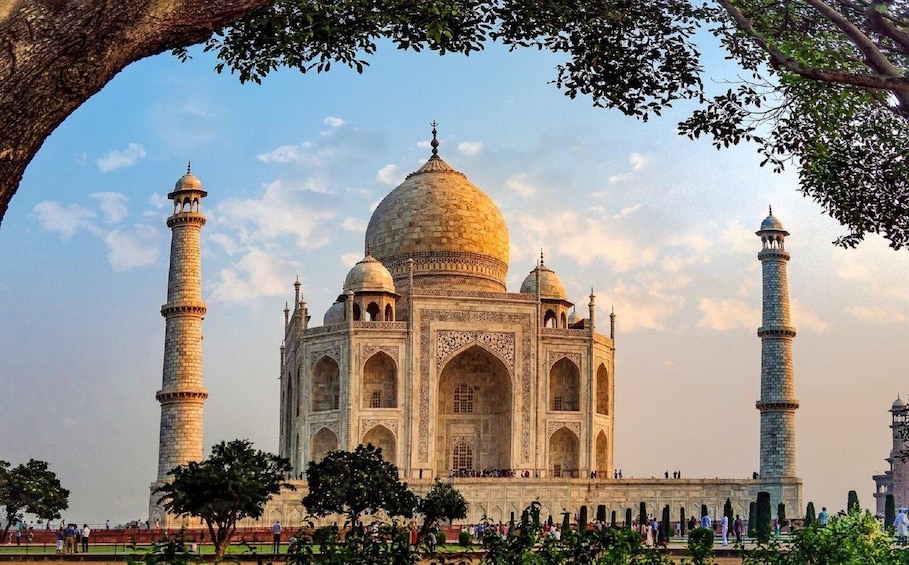 The Taj Mahal with four minarets and a large central dome, surrounded by trees and visitors. 1