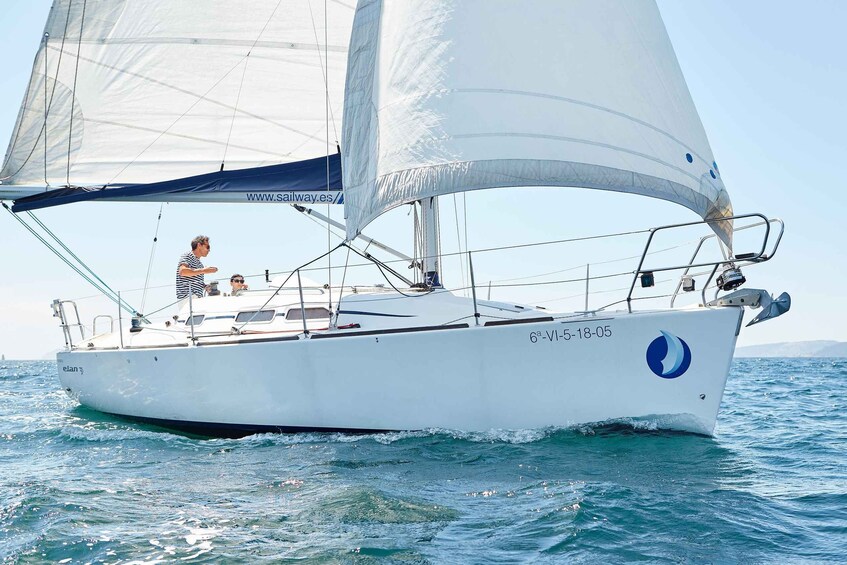 A sailboat with a white hull and blue logo sailing on blue waters. 4