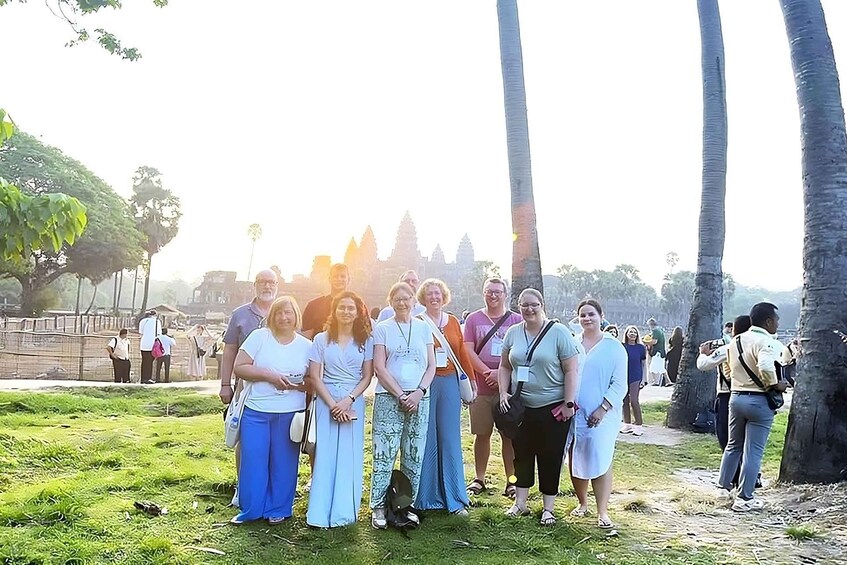 A group of people standing in a grassy area with palm trees and a temple in the background. 5