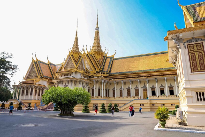 A grand palace with ornate golden roofs and multiple spires, surrounded by a paved courtyard with a large tree and trimmed hedges. 4