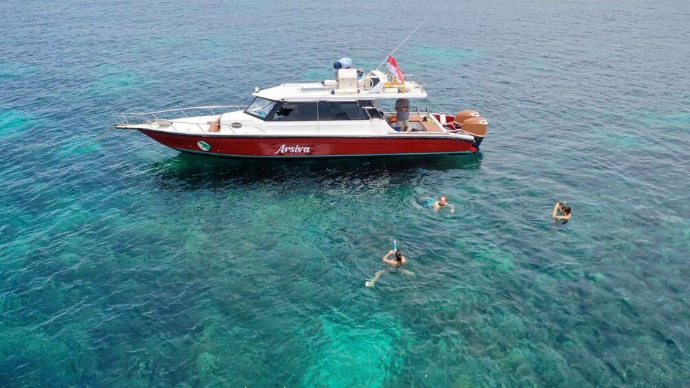 A boat named 'Arsiva' on clear turquoise water with four people swimming nearby. 5