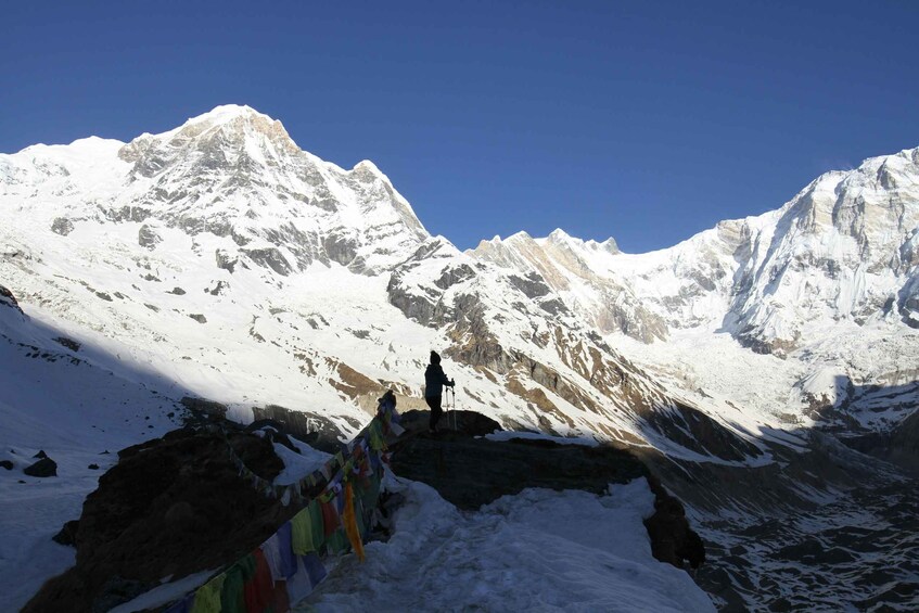 A person standing on a snow-covered peak with a mountain range in the background. 2