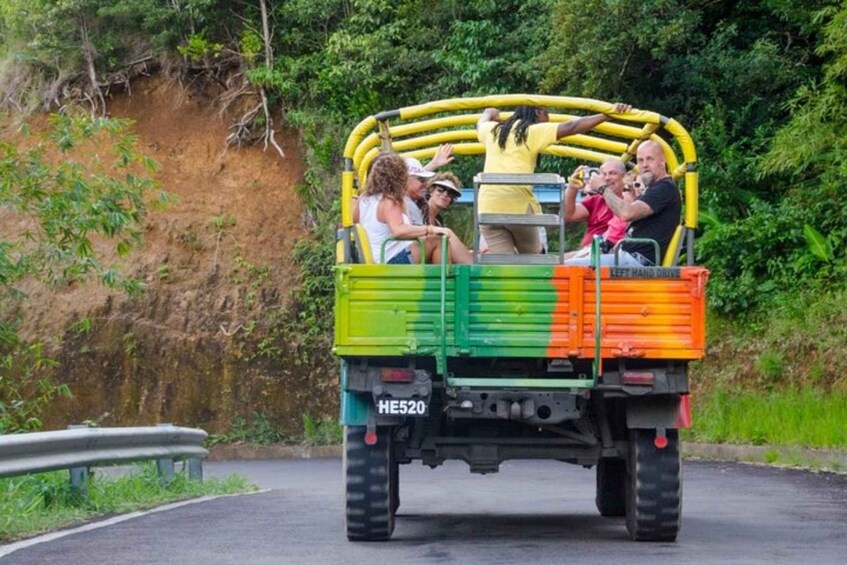 A colorful truck with passengers, a guardrail, and a dirt embankment. 3