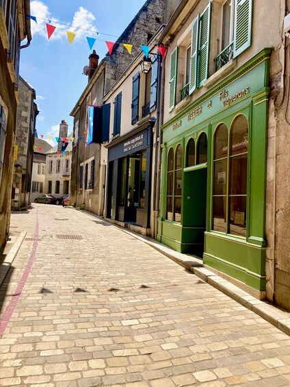 A cobblestone street lined with historic buildings, one with a green facade and arched windows, and colorful triangular flags strung above. 2