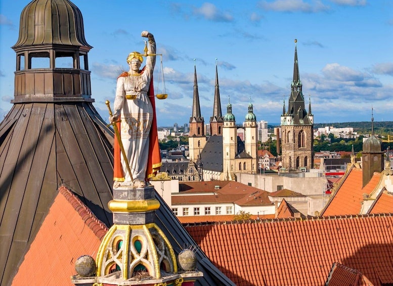 A statue of a figure holding scales on a building's roof, with a cityscape featuring spires and domes in the background. 3