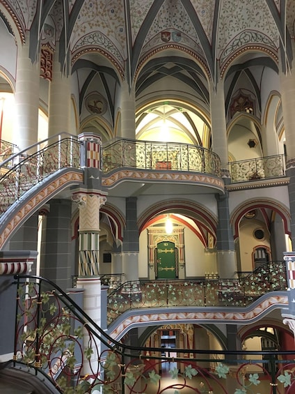 A grand interior with ornate arches, a staircase with floral decorations, and a green door marked '123'. 2