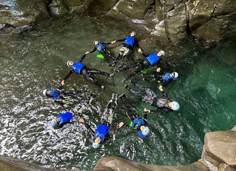 A group of people in blue wetsuits and helmets floating in a circular formation in a body of water surrounded by rocky terrain. 2