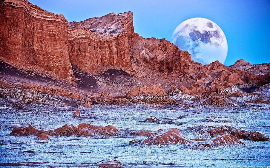 Un paisaje desértico con formaciones rocosas estratificadas y una luna grande en el cielo. 1