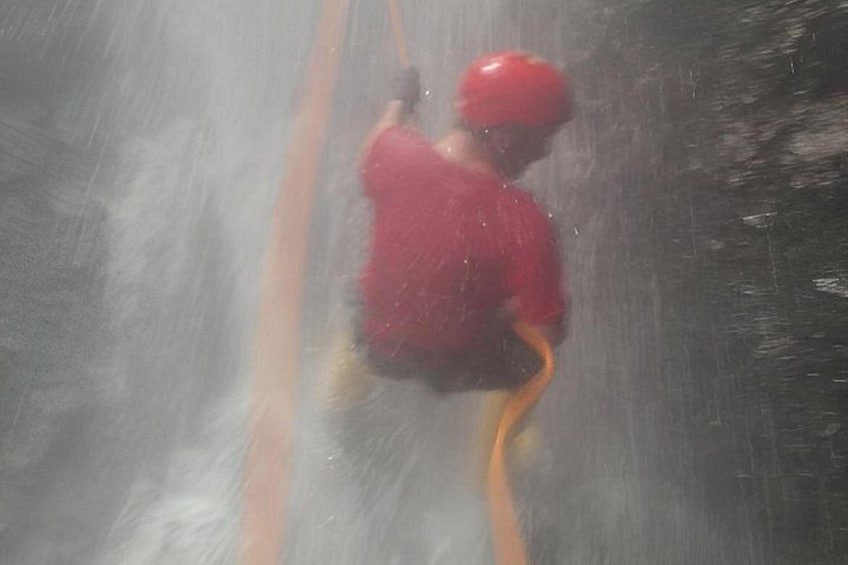 A person in a red shirt and helmet climbing a rope. 2