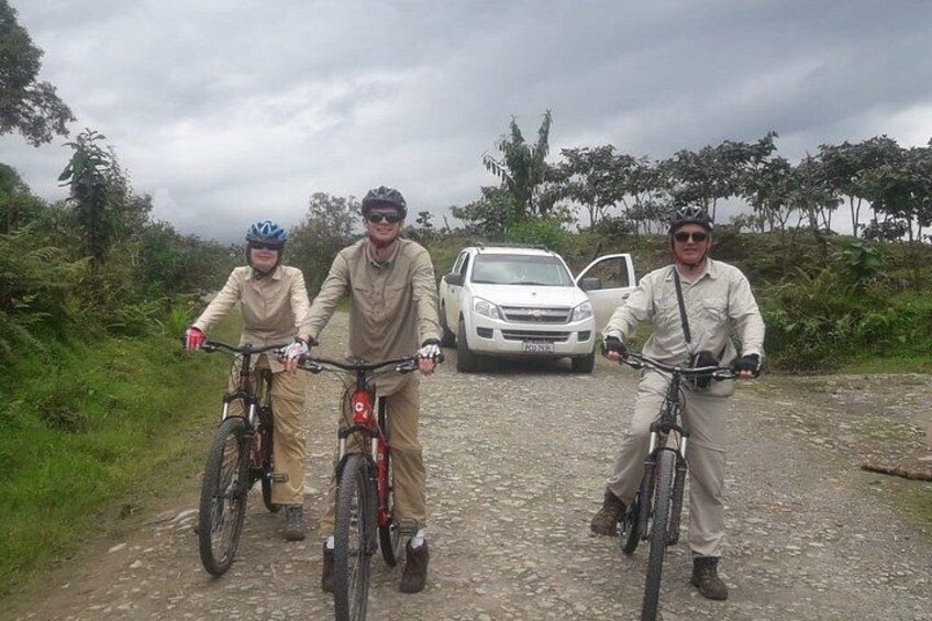 Three people on bicycles on a gravel path with a white car parked behind them. 3