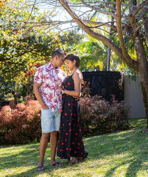 A couple standing in a garden with lush greenery and a stone wall in the background. 3