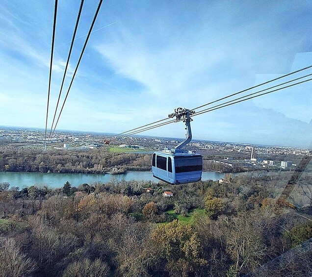 A cable car suspended over a river, with a cityscape and mountains in the background. 3