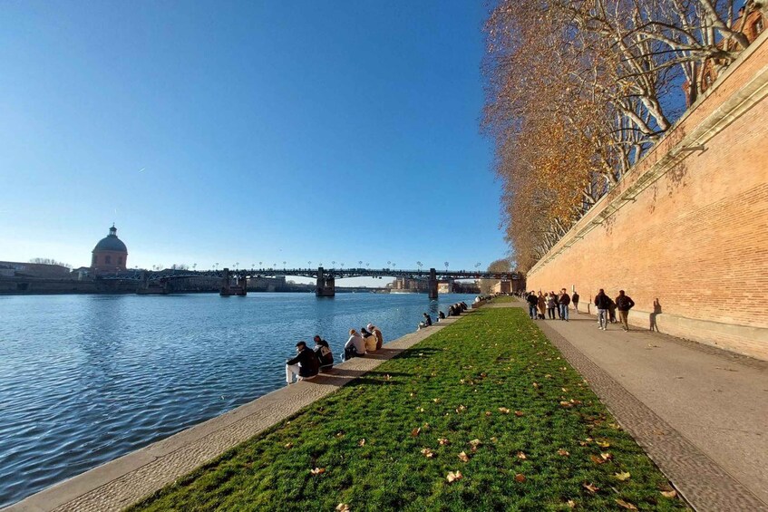 A riverside walkway with people walking and sitting, a bridge in the background, and a domed building. 4