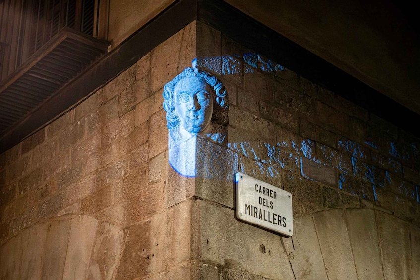 A stone wall with a carved bust and a street sign reading 'Carrer dels Miralles.' 1