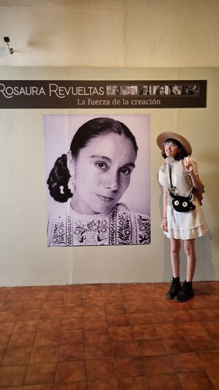 A person standing in front of a wall with a large portrait and a sign that reads 'ROSAURA REVUELTAS La fuerza de la creación.' 3