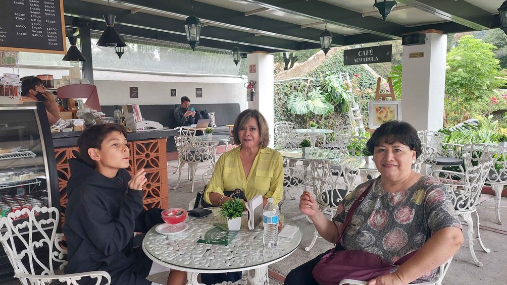 Three people seated at a round table with a menu board in the background. 4