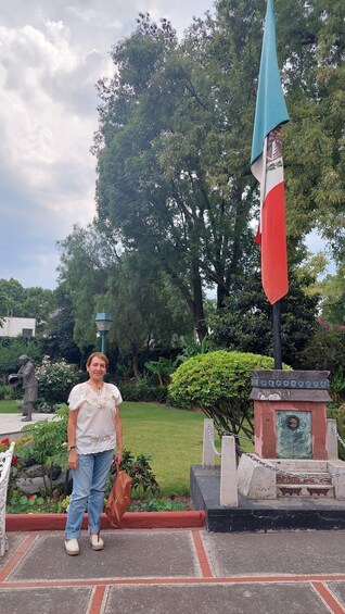 A person standing in front of a flagpole with a statue and a plaque in a park. 2