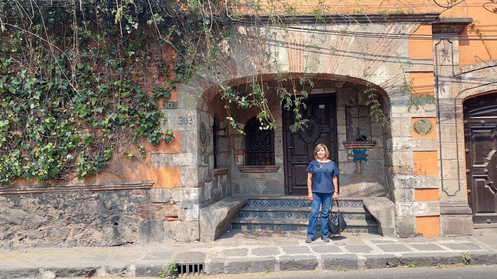 A woman standing in front of a building with a stone archway, a door, and a window. 5