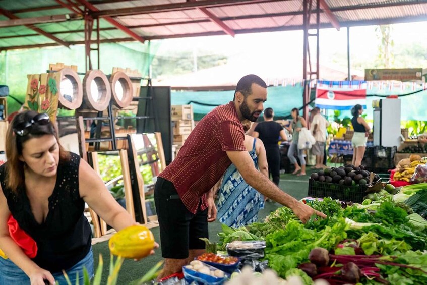 A market with people shopping, fresh produce, and wooden sculptures. 3