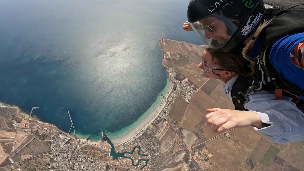 A person skydiving over a coastal area with a clear view of the coastline, a river, and urban development. 3